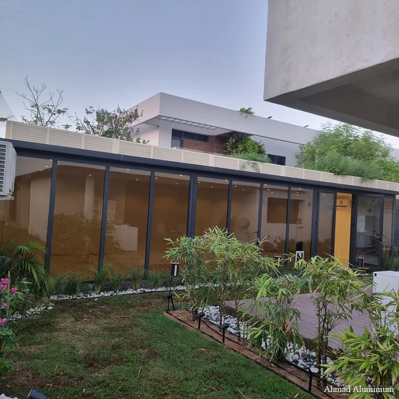 Modern outdoor glass room extension with black aluminium frames and sliding doors in a Dubai villa garden.