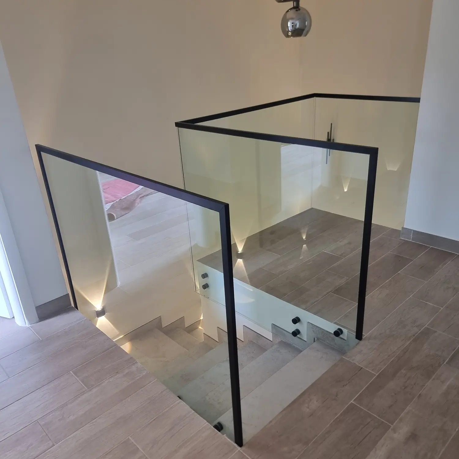 Sleek side-mounted glass railing with stainless steel standoffs for a modern floating staircase effect.