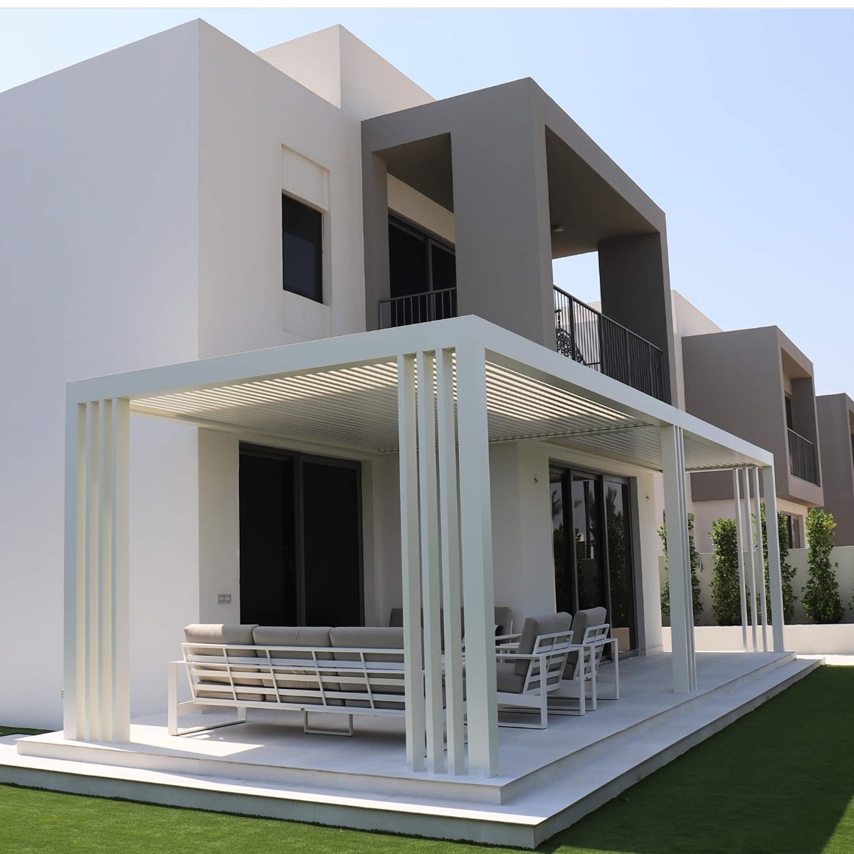 Custom wall-mounted powder-coated aluminium pergola extending over a modern villa patio setup.